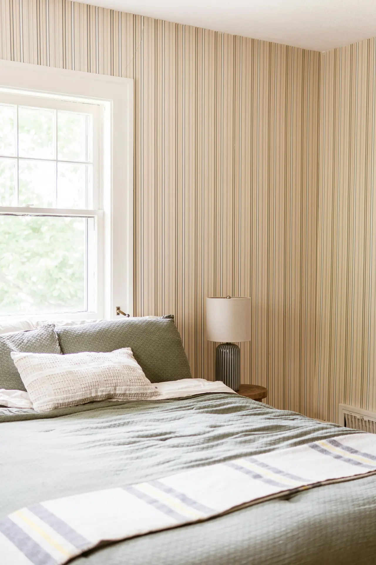 Small bedroom with green bedding and striped wallpaper